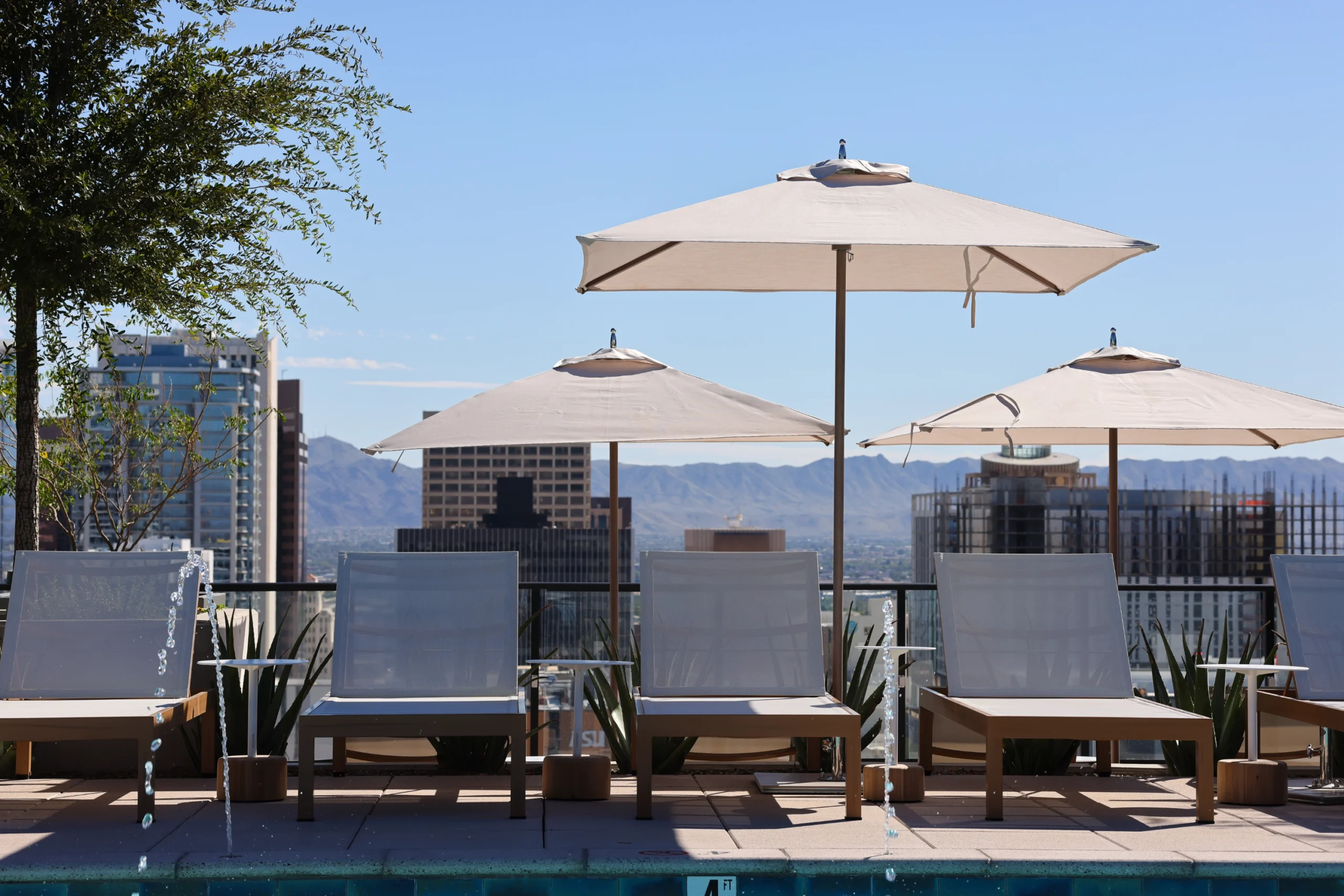 Rooftop pool deck in a mixed-use housing tower with lounge chairs, shade umbrellas, and city and mountain views