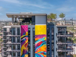 Mixed-use housing tower with residential balconies, rooftop amenities, and large-scale public art mural in an urban high-rise development