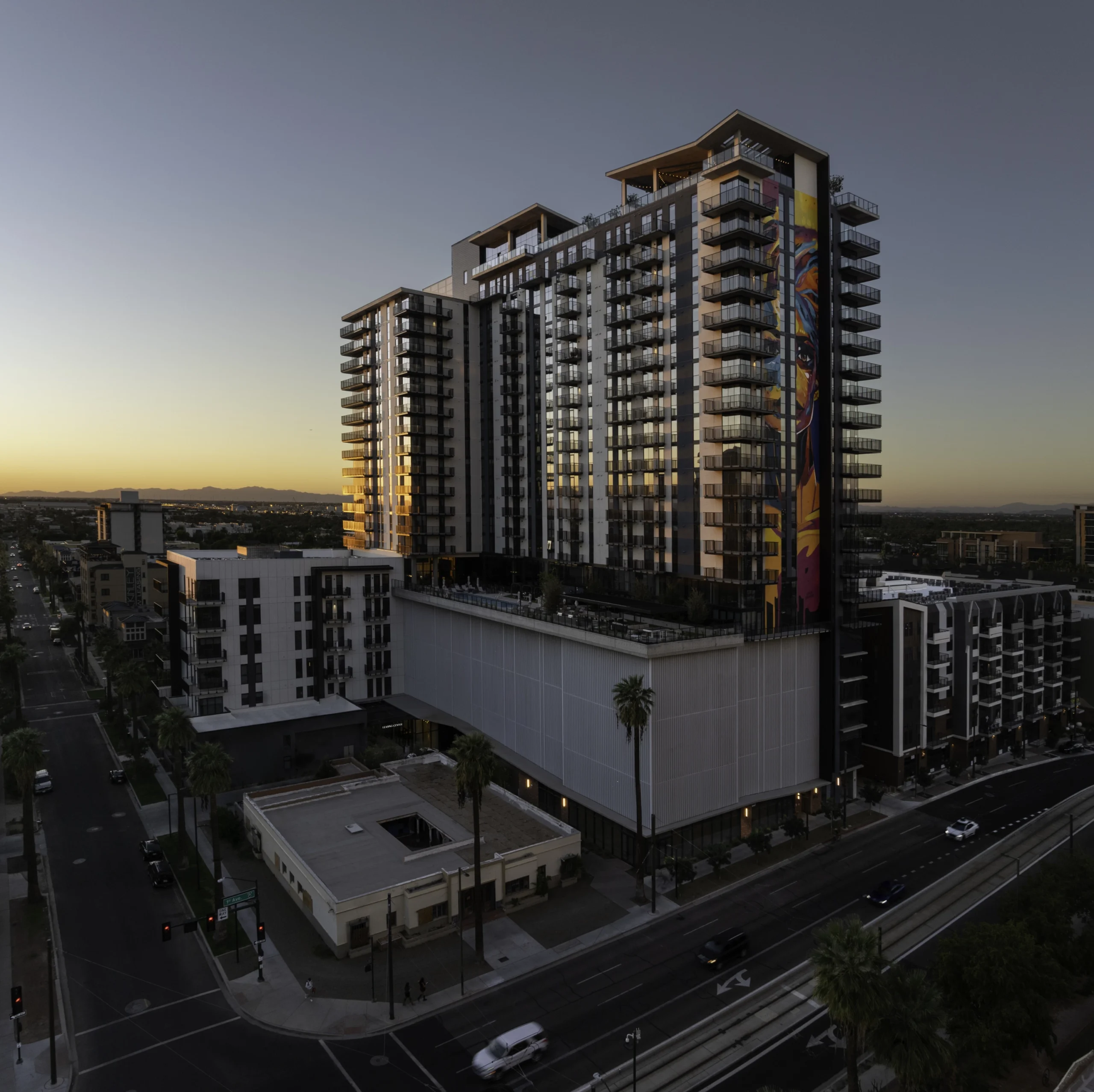 Mixed-use residential development with high-rise apartments above a multi-story podium, activating a downtown urban streetscape at sunset