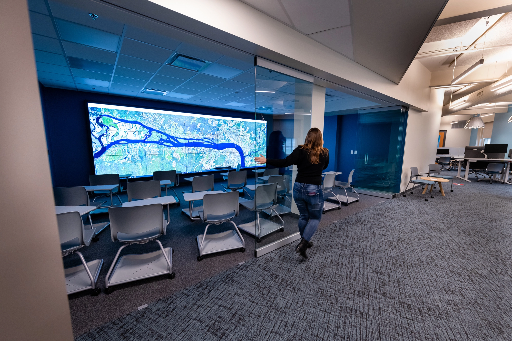 Flexible learning space with moveable glass wall opening in library in front of large screen and flexible desk seating
